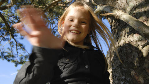 Ein lachendes Kind winkt in die Kamera. Es ist draußen in der Natur