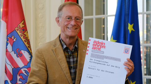 Staatsminister Axel Wintermeyer hält den Förderbescheid aus dem Programm "dein ehrenamt" in den Händen und lächelt.