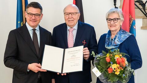 Ministerpräsident Rhein neben den Eheleuten Gerling. Er überreicht die Urkunde und das Verdienstkreuz, alle lächeln.