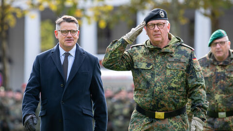 Ministerpräsident Rhein steht neben einem Bundeswehr-Soldaten, der salutiert