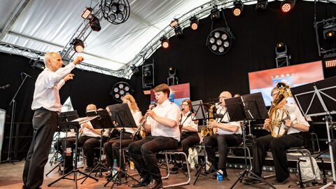 Mehrere Personen stehen und sitzen auf einer Bühne und spielen Instrumente.