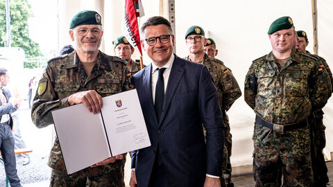Ministerpräsident Boris Rhein hält mit einem Mann von der Bundeswehr eine Urkunde in die Kamera. 