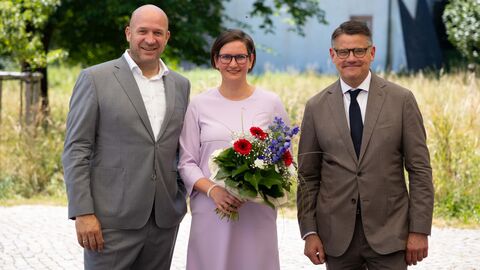 Zwei Männer und ne Frau lachen in Kamera. die Frau hält einen Blumenstrauß.