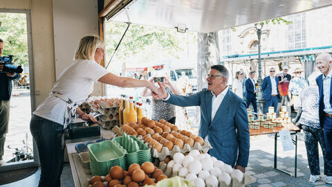 Mann an Marktstand gibt Frau die Hand.