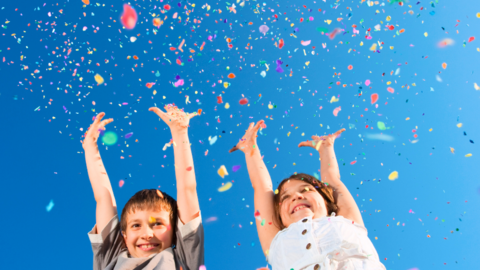 Zwei fröhliche Kinder werfen buntes Konfetti in die Luft.