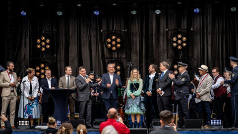Ministerpräsident Boris Rhein, der Chef der Staatskanzlei Benedikt Kuhn und das Hessentagspaar stehen auf einer Bühne zusammen mit zahlreichen Musikern