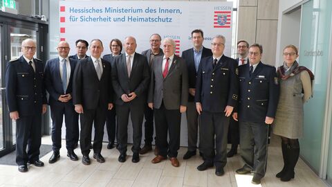 Innenminister Roman Poseck steht mit dem Präsidenten der IGMK, Herrn Dietmar Jerger, Vertretern der Karnevalsvereine, des HMdI und der Polizei in einem Raum zum Gruppenfoto aufgestellt.