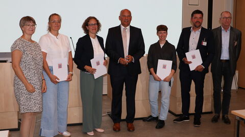 Mehrere Personen stehen vor einer Leinwand. Einige halten eine Mappe mit dem Hessenwappen darauf.